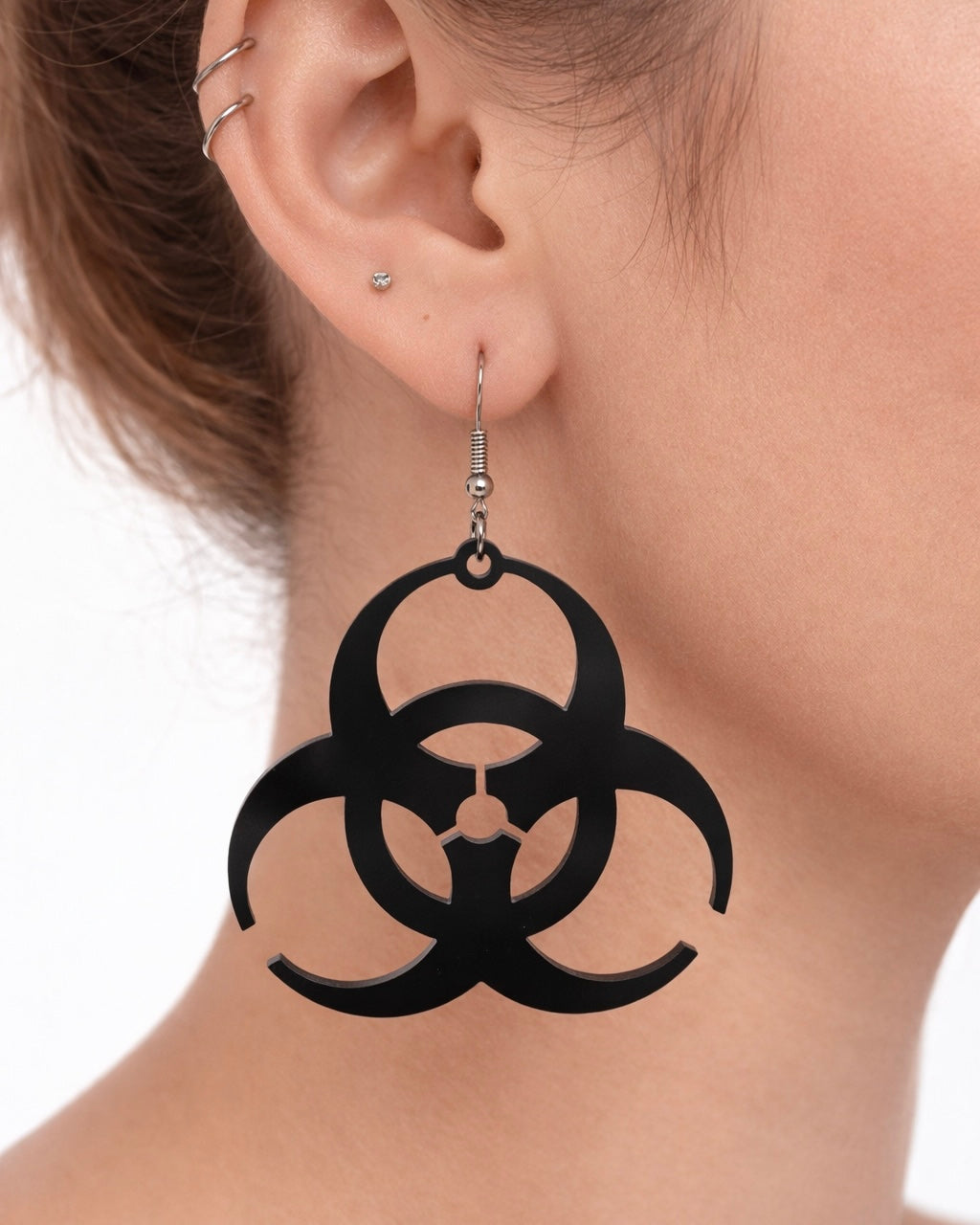 Black biohazard symbol earrings worn by a person on a white background