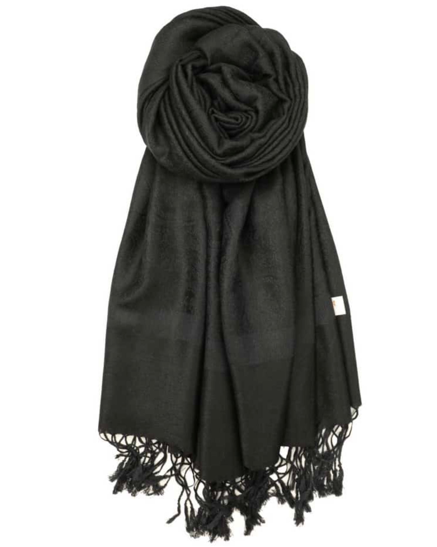 A black pashmina with paisley pattern and fringes spread out on a plain surface.