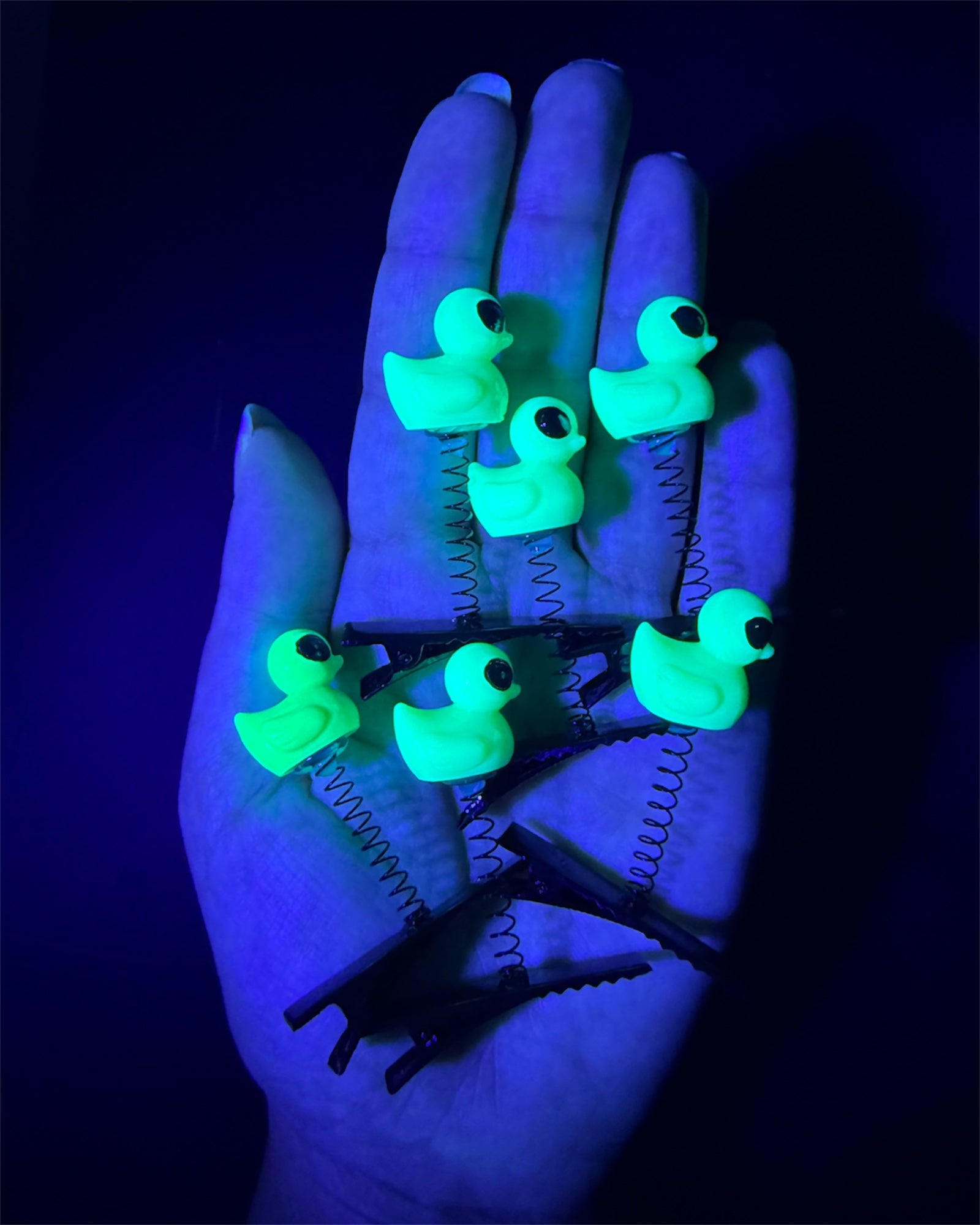 Glowing green alien duck-shaped sprout clips on a hand against in a blacklight room.
