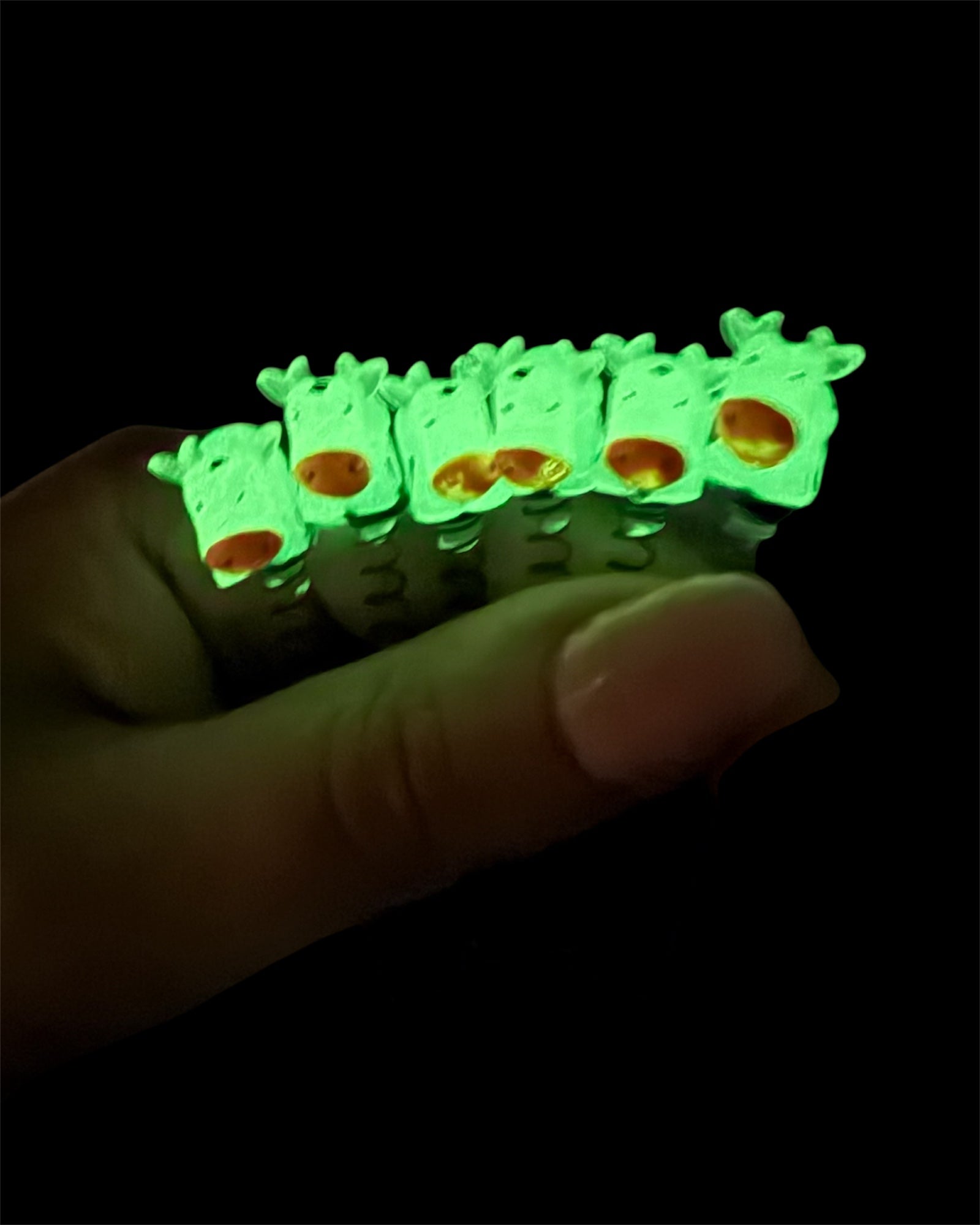 Glowing green cow clips held by a hand against a dark background