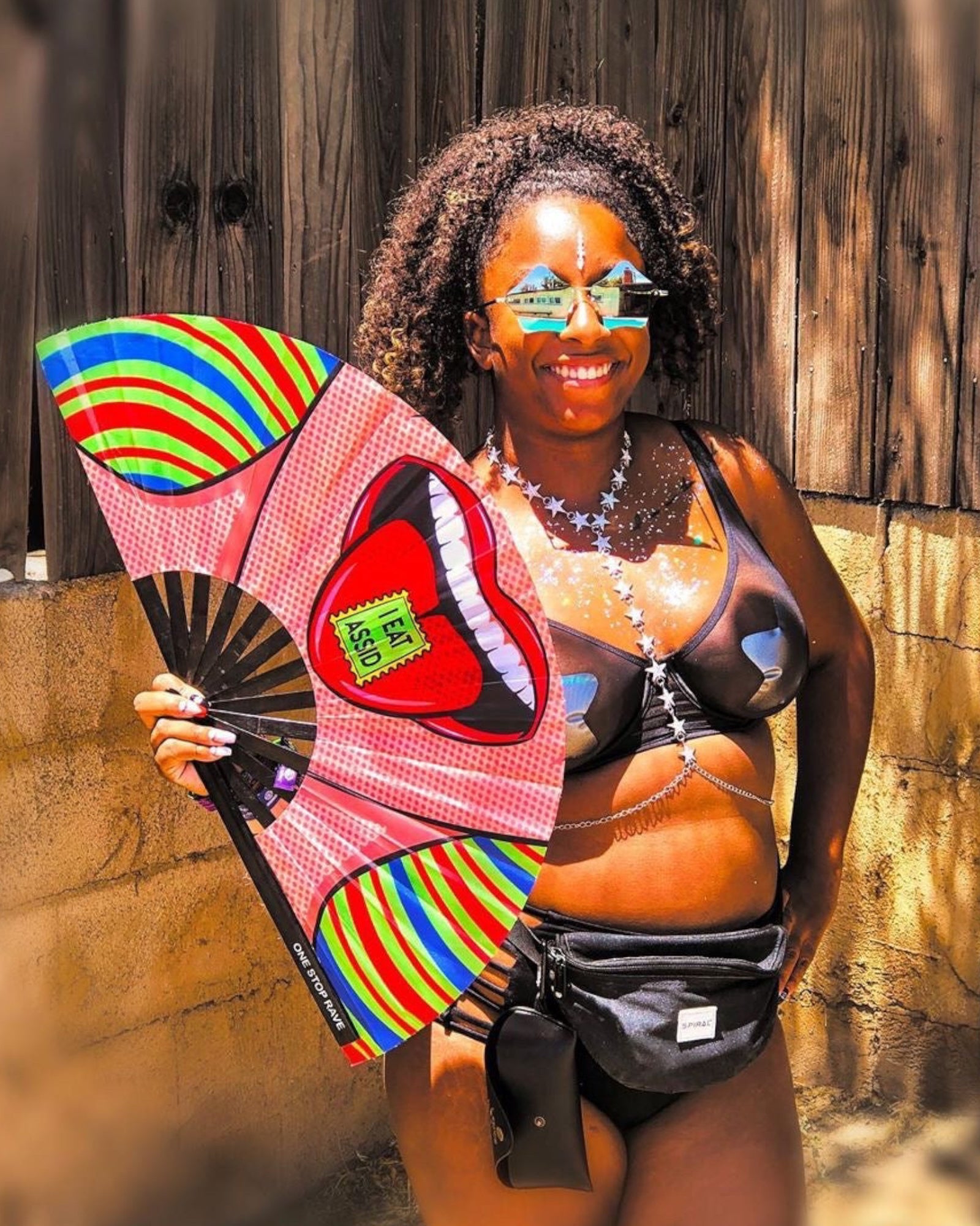 I Eat Assid hand fan held at festival by woman in rave outfit