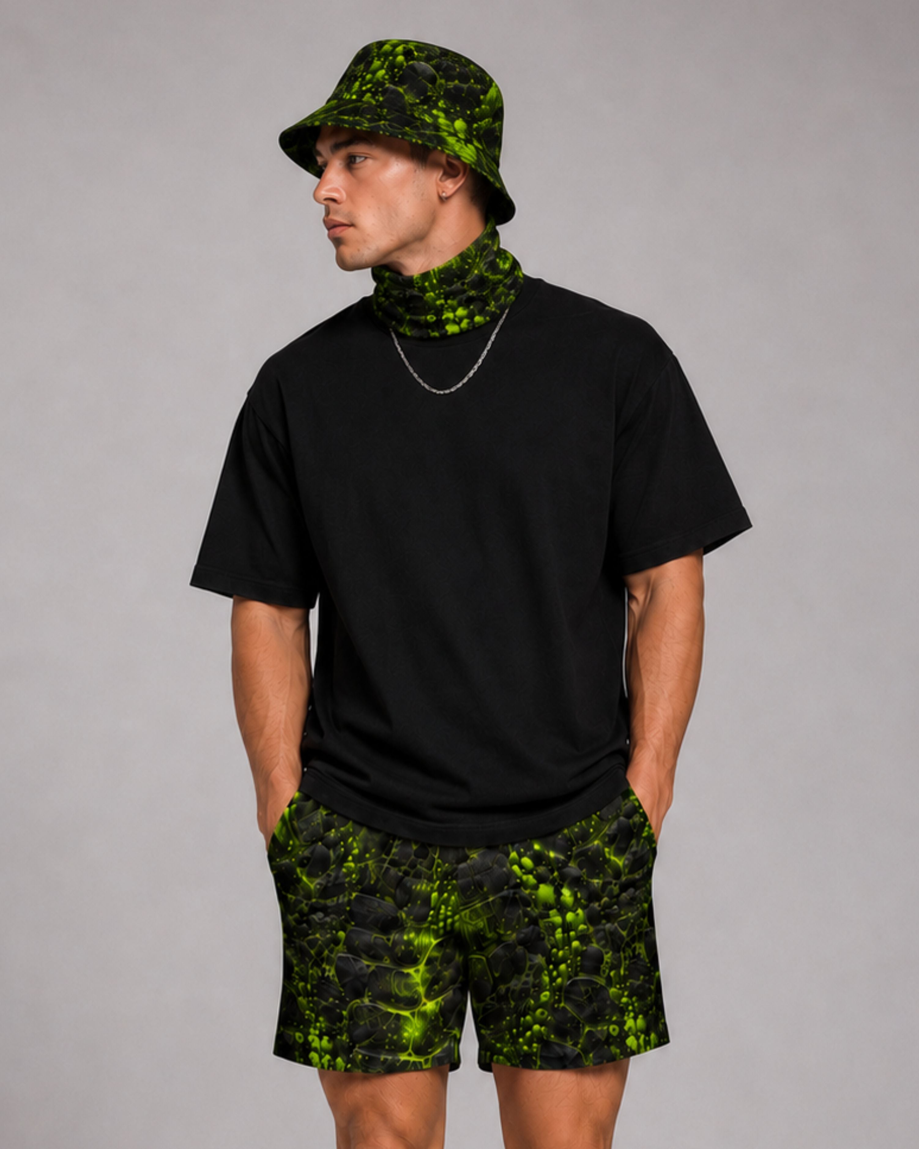 Man wearing a black oversized tee with a green and black cracked-texture bucket hat, bandana, and matching shorts.