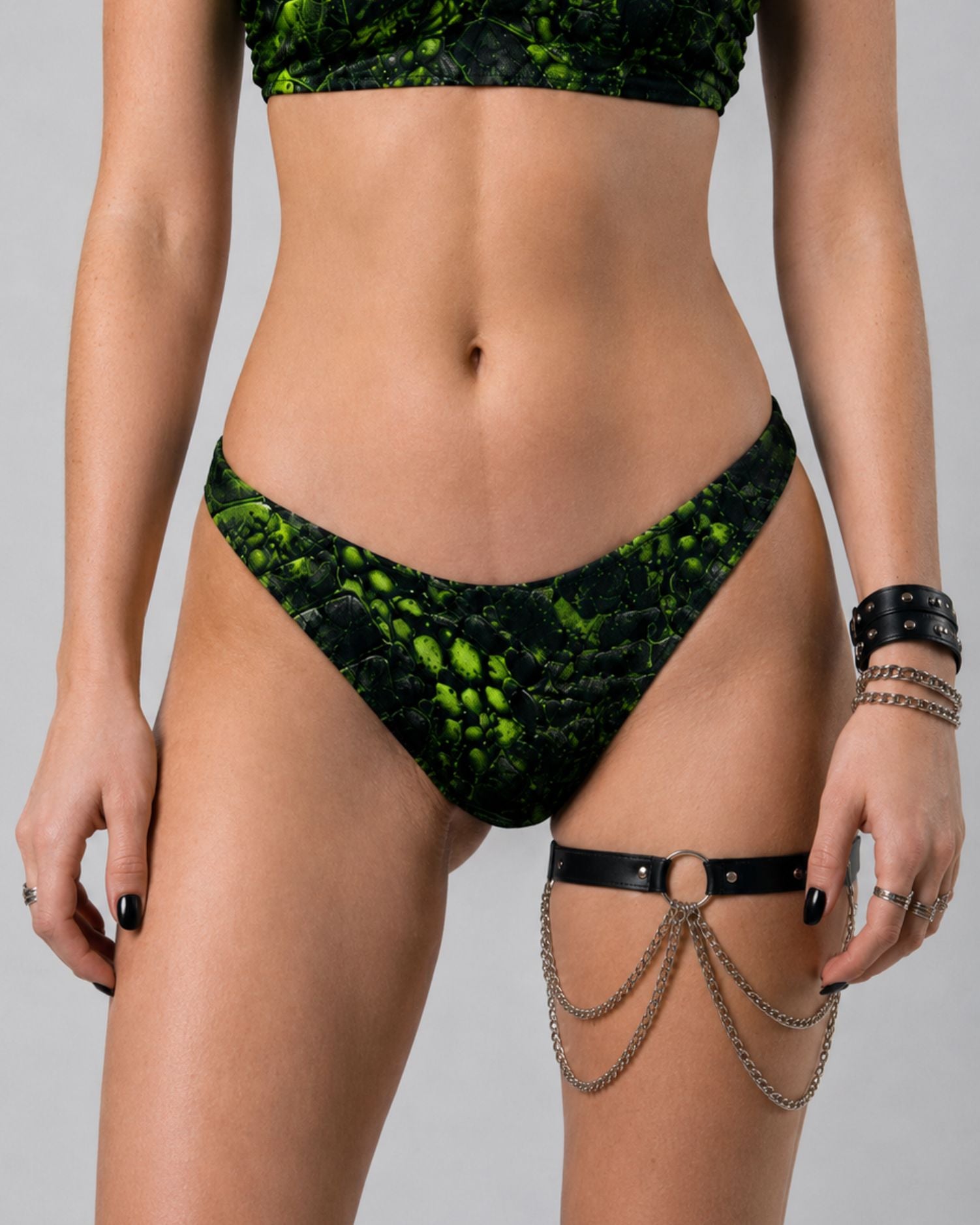 Front view of black and neon green cracked-texture V-cut bikini bottom, styled with a chain-detail leg harness.