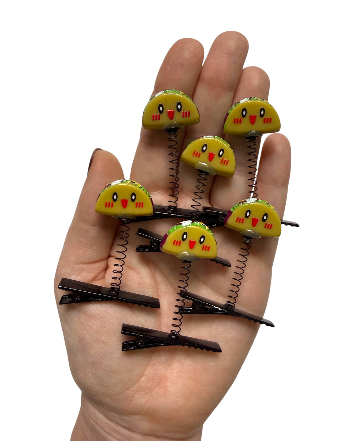 Five small yellow taco-shaped spring clips with cartoon faces are arranged on an open hand against a plain white background.