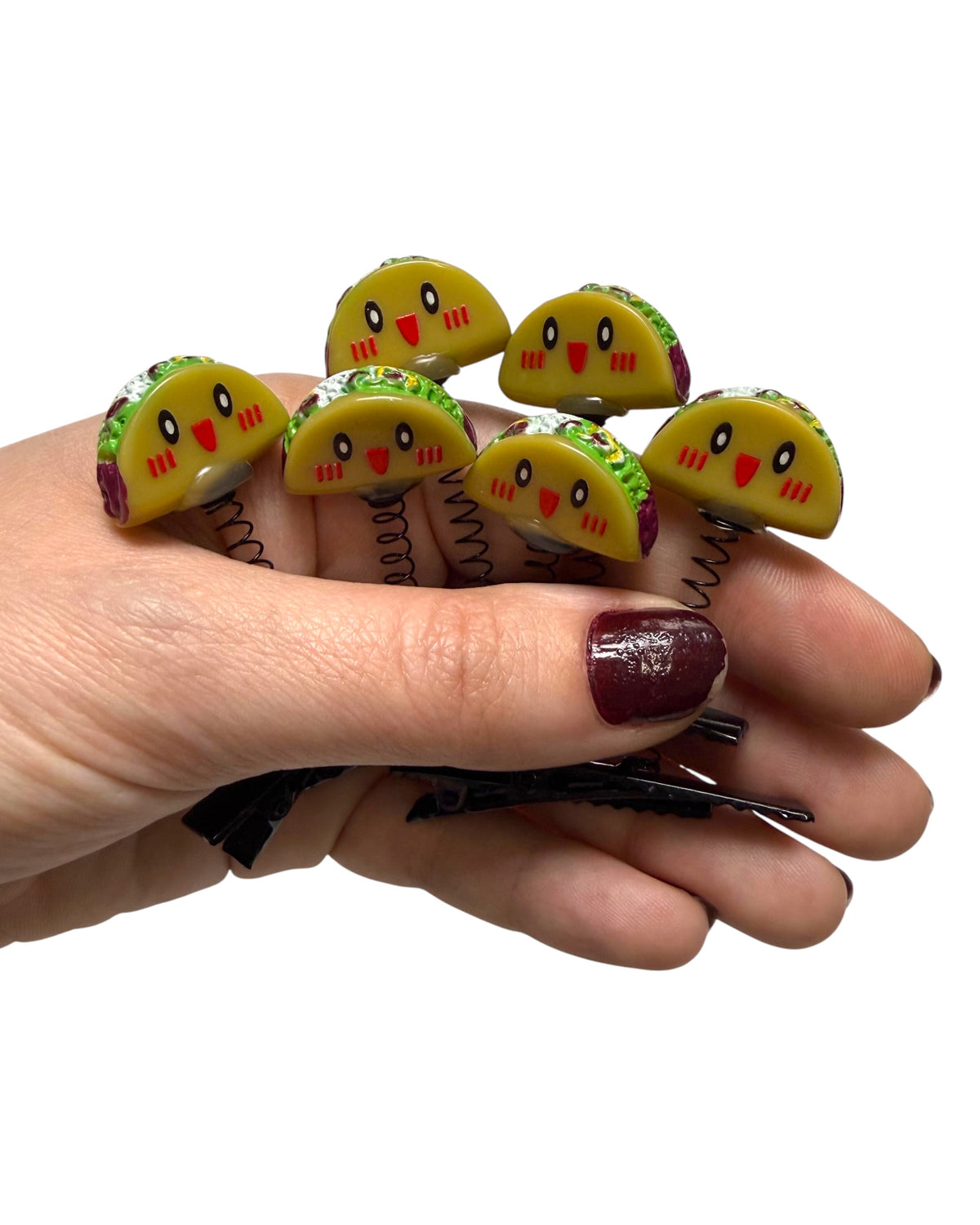 A hand holding a set of spring-loaded taco-shaped hair clips with cute cartoon faces, shown against a plain white background.
