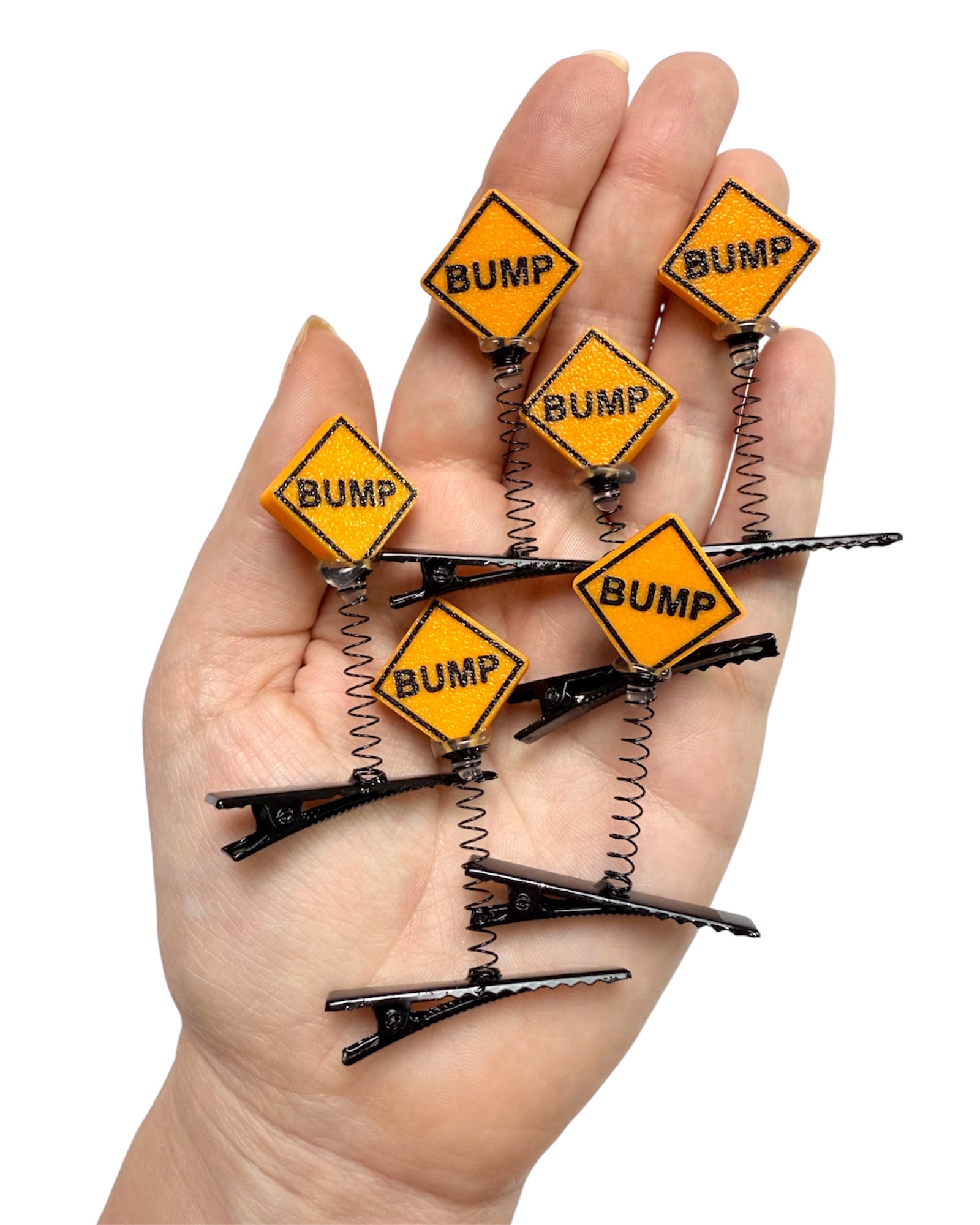 Hand holding multiple hair clips with 'BUMP' signs on a white background