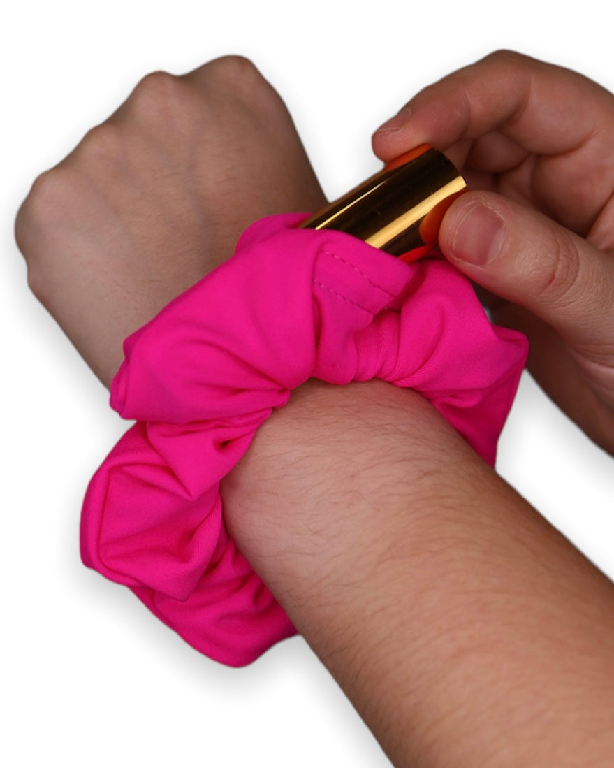 Hot Pink Stashie in Use – A wrist shot of the hot pink stash scrunchie, showcasing the hidden Velcro® pocket being opened to reveal a lipstick inside.