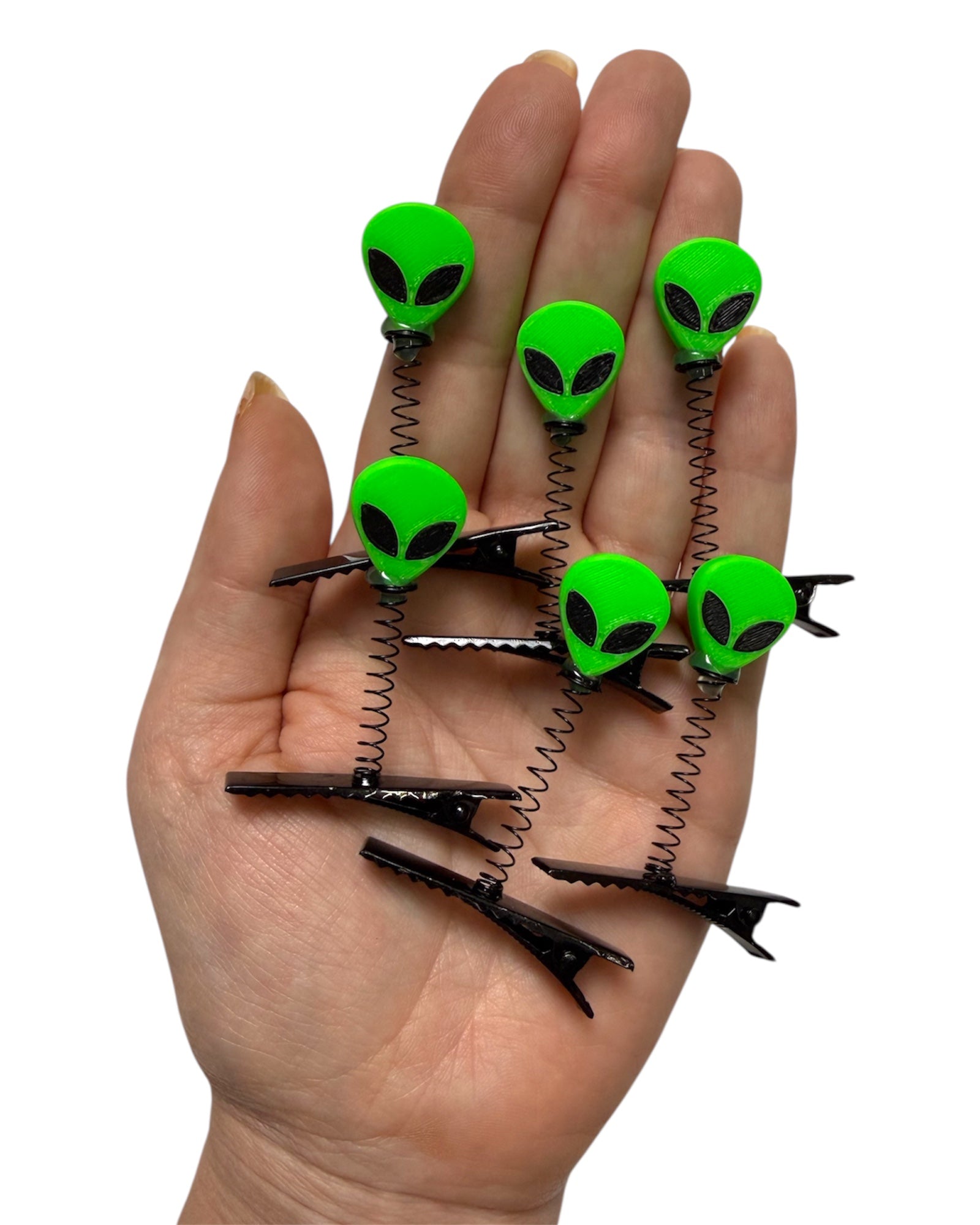 Hand holding Fluorescent green alien-shaped hair clips on a white background