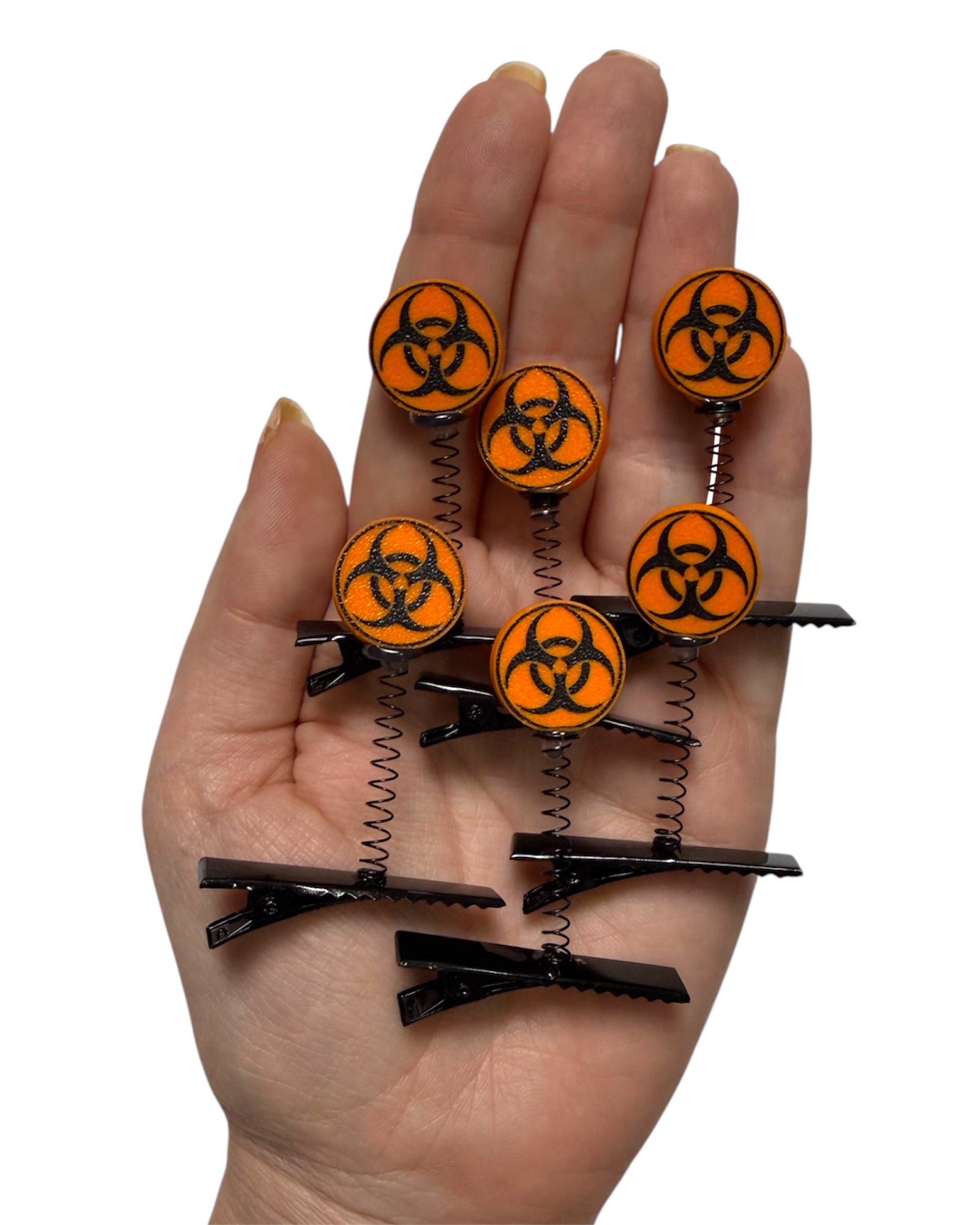 Hand holding hair clips with biohazard symbol design on a white background.