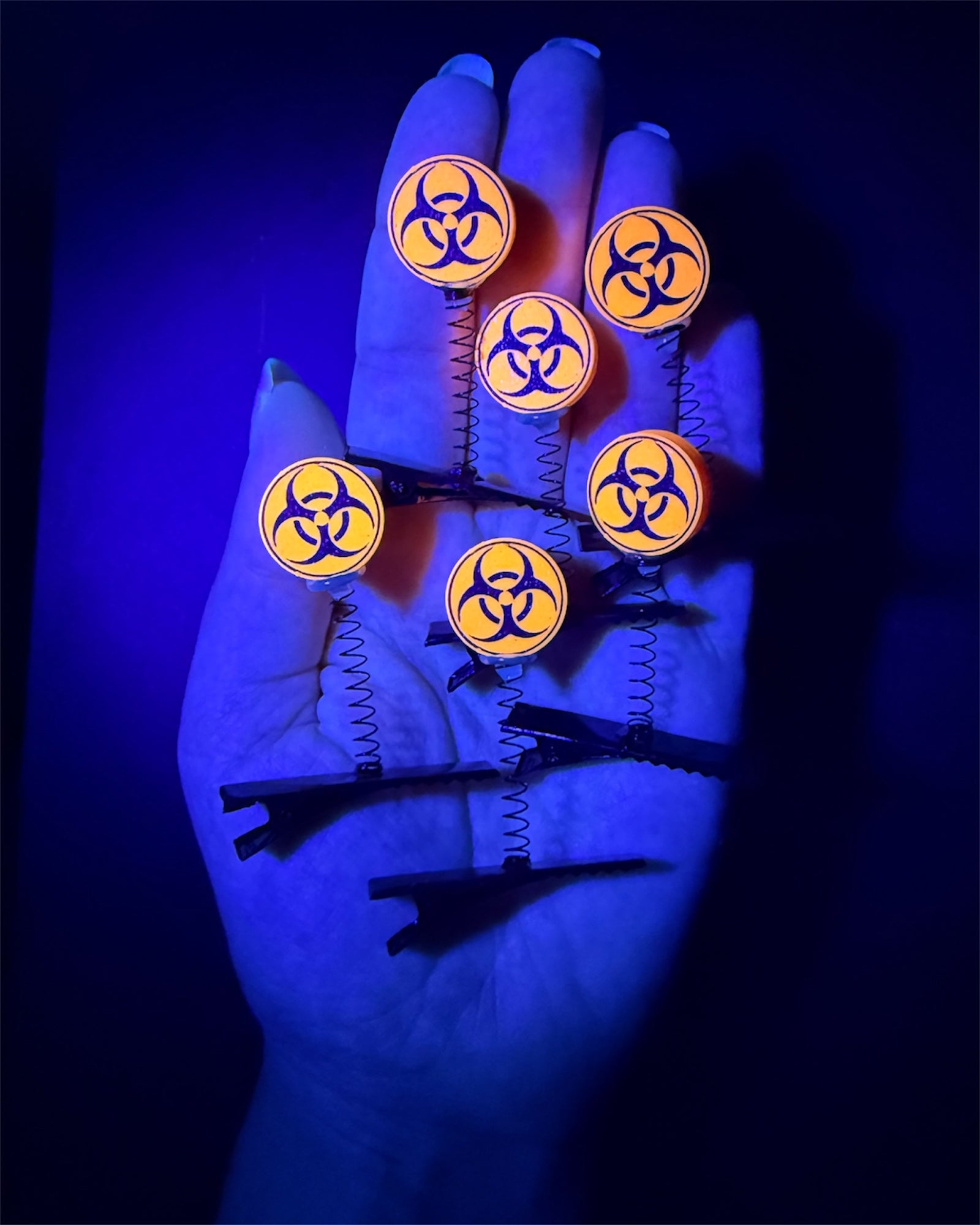 Glowing biohazards sighns attached to hair clips under black light making festival sprouts.