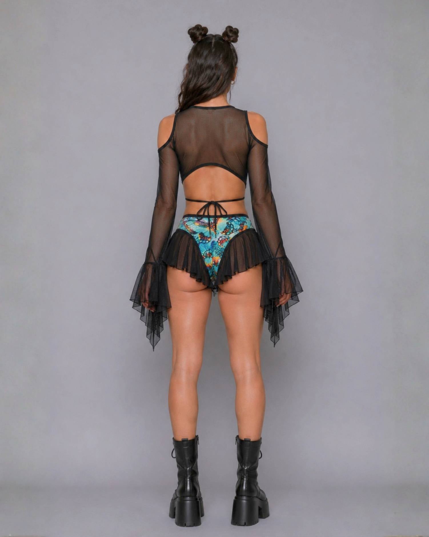 Back view of black sheer mesh cold-shoulder top with bell sleeves over a blue butterfly-print high-waisted bottom with mesh ruffle trim.