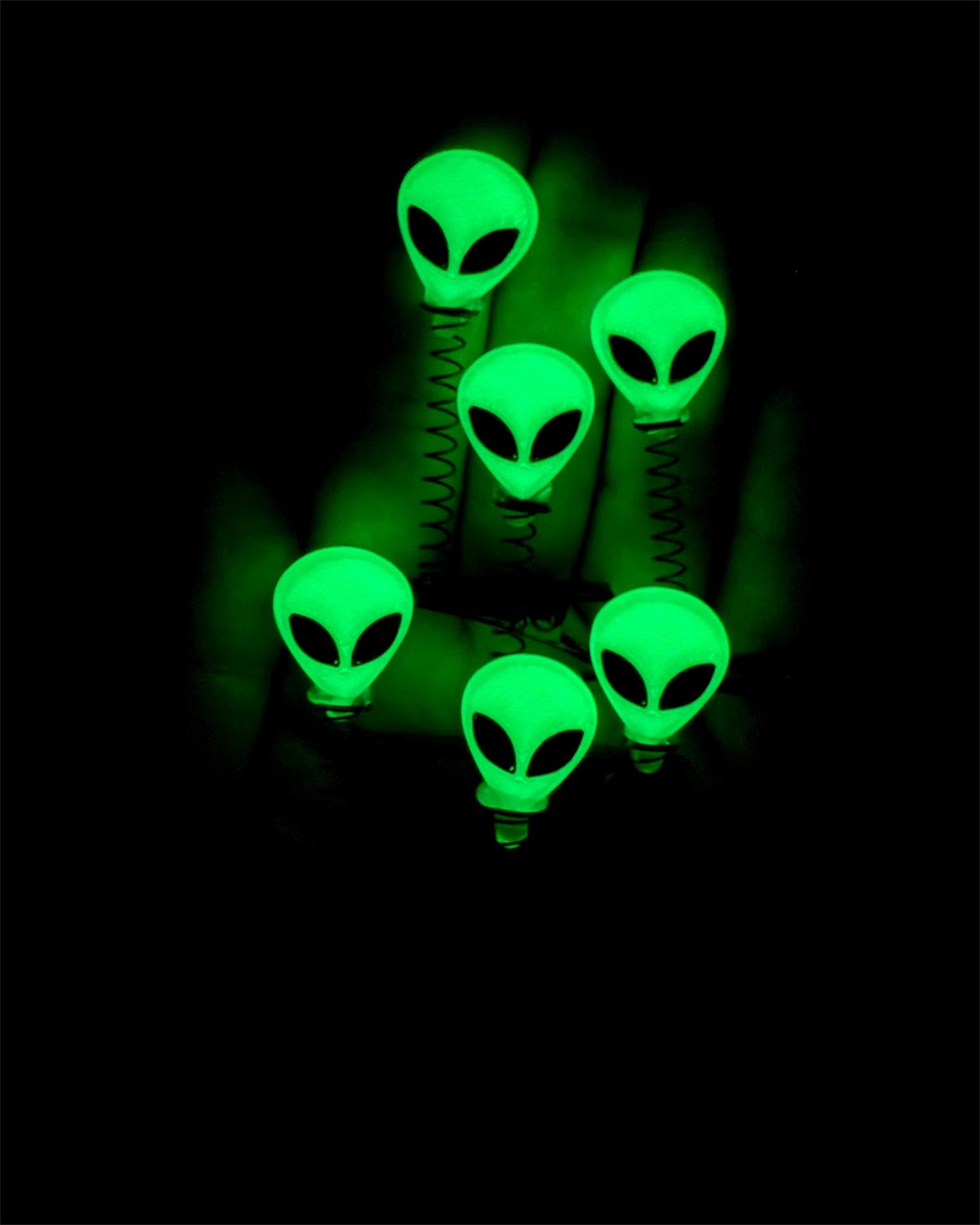 Green alien-shaped hair clips glowing in the dark in a room with lights turned off. 