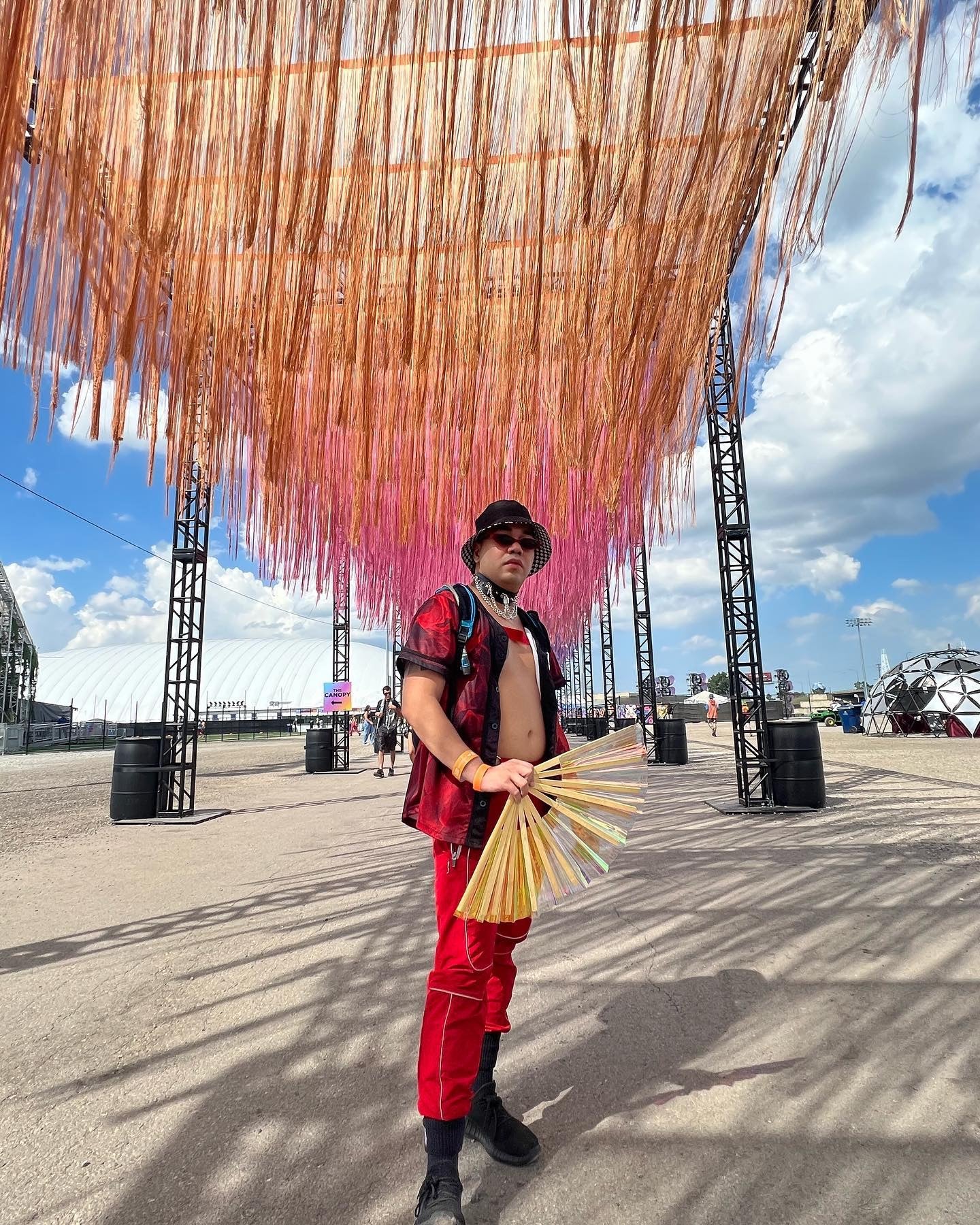 Person holding open Iridescent Vinyl Hand Fan outdoors at a festival.