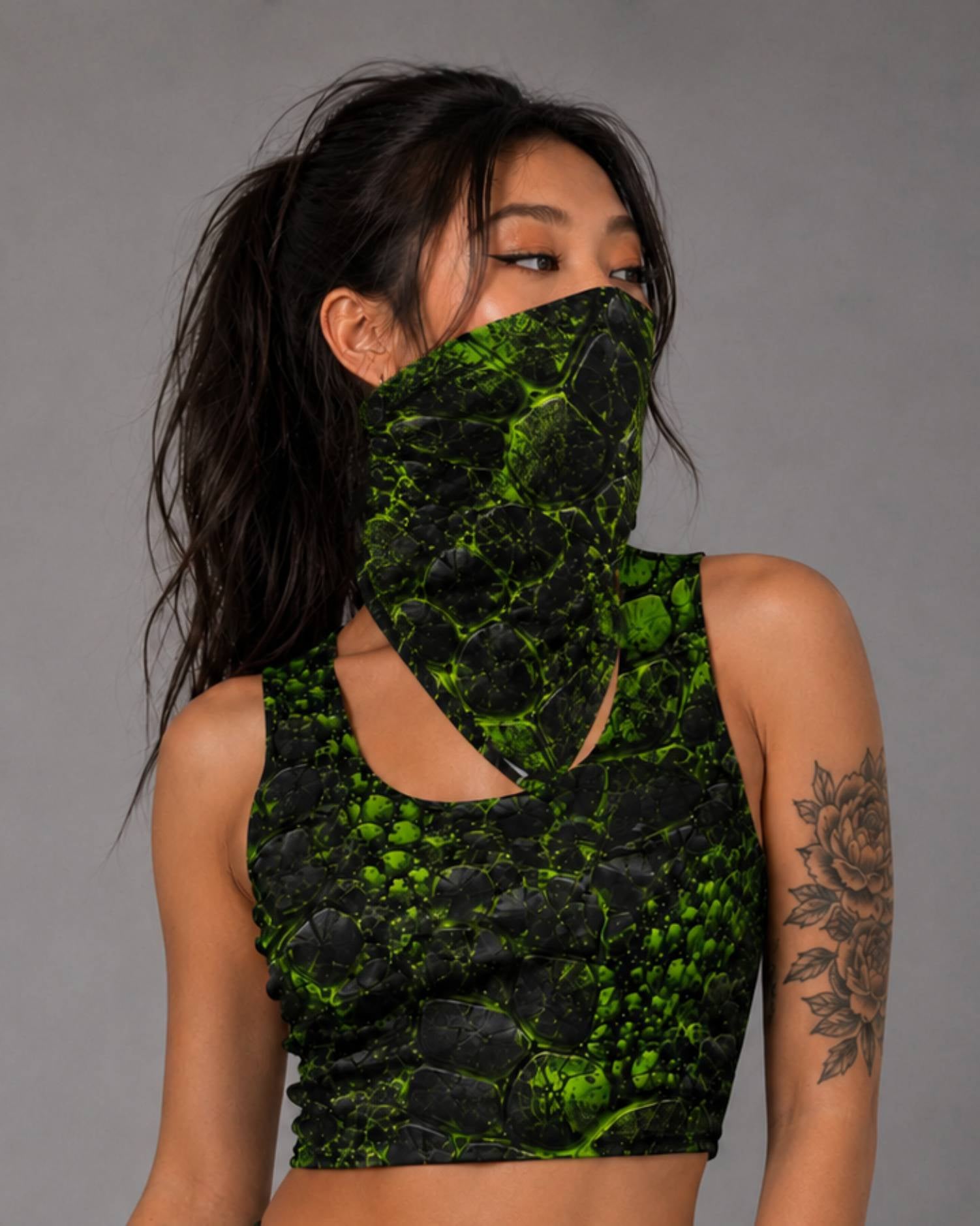 Woman wearing a black and neon green cracked-texture bandana as a face covering with a matching ravage cutout crop top.