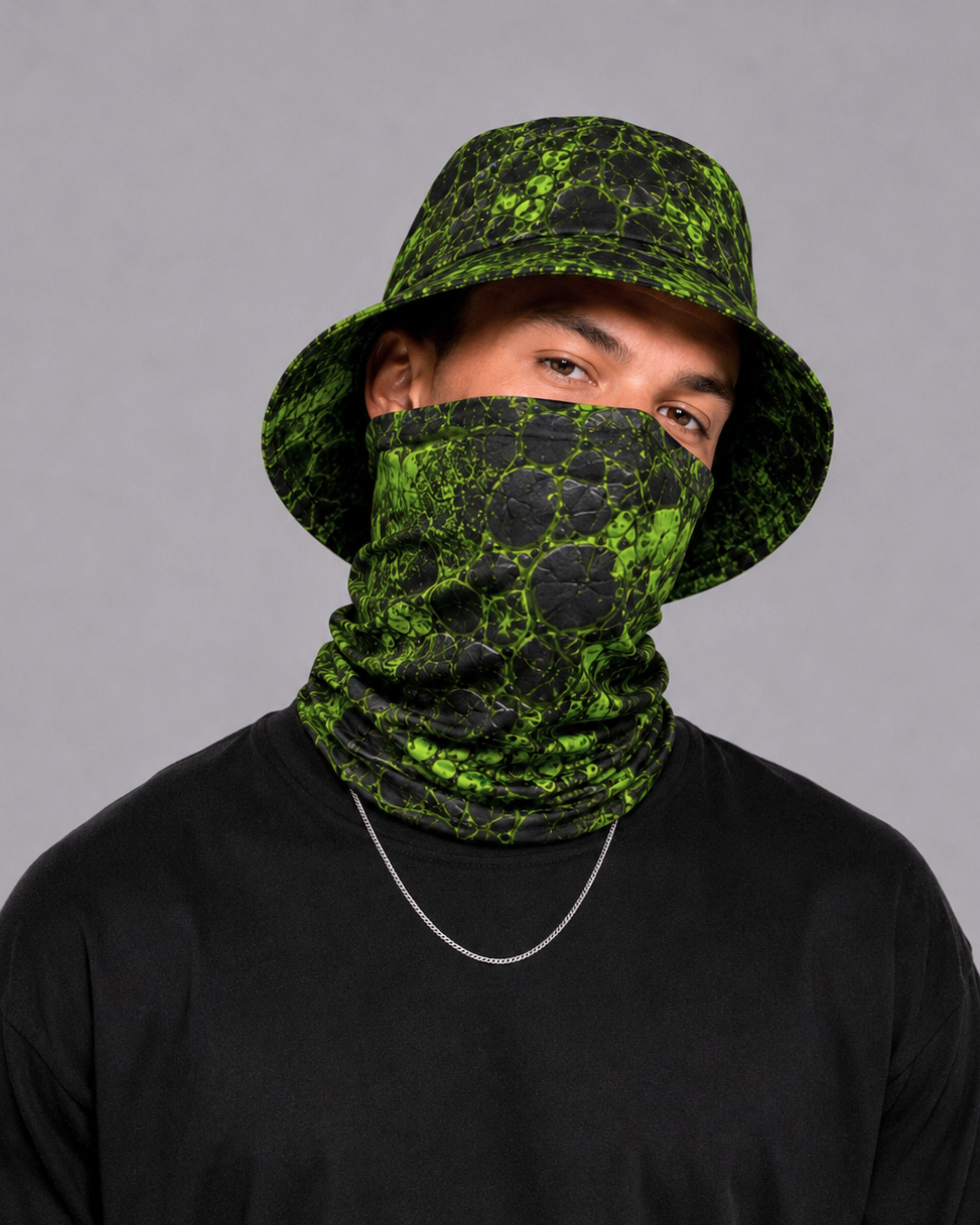 Man wearing a black and neon green cracked-texture bucket hat and matching bandana face covering with black long sleeve shirt.