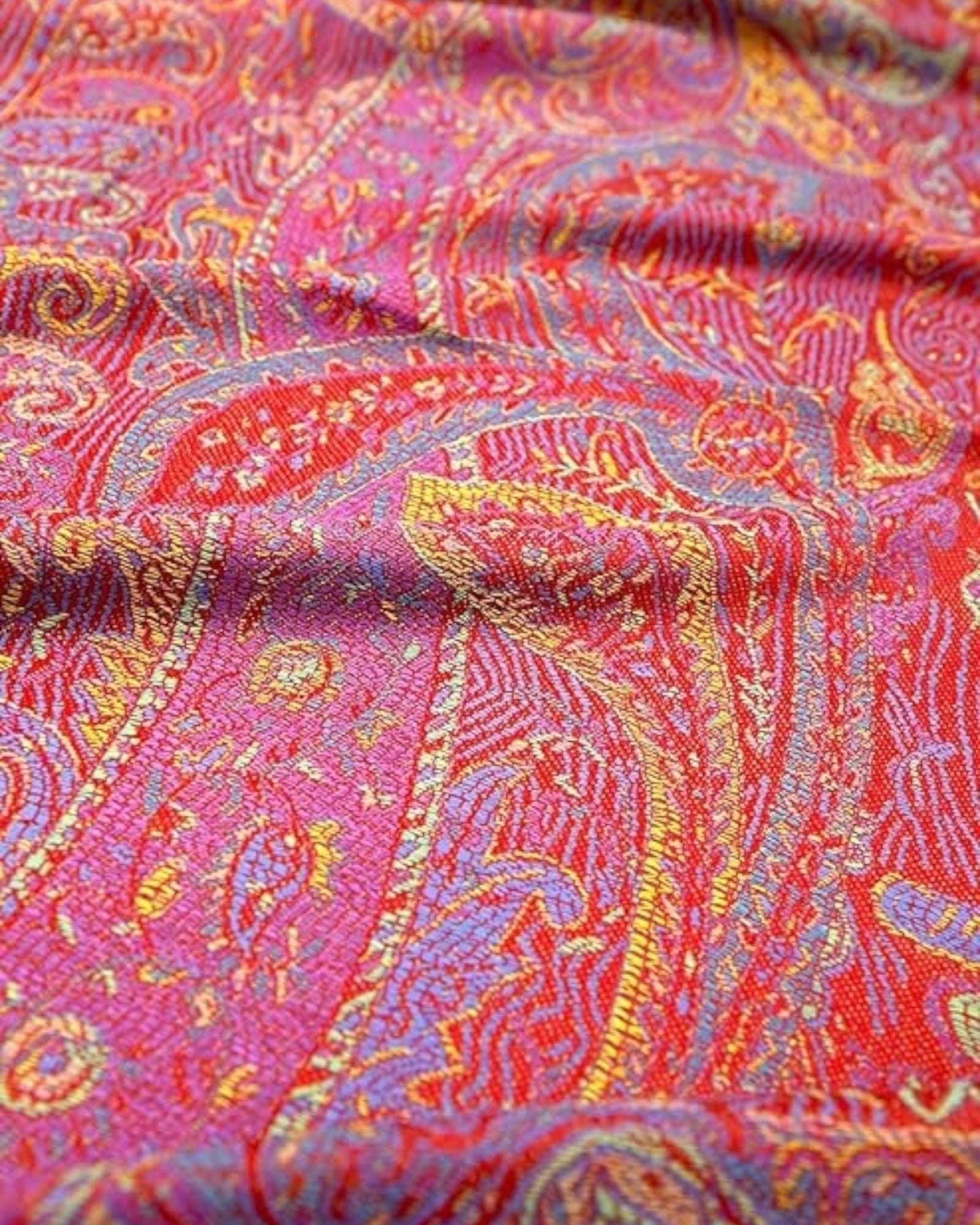 A red pashmina with paisley patterns close up displayed on a white background.