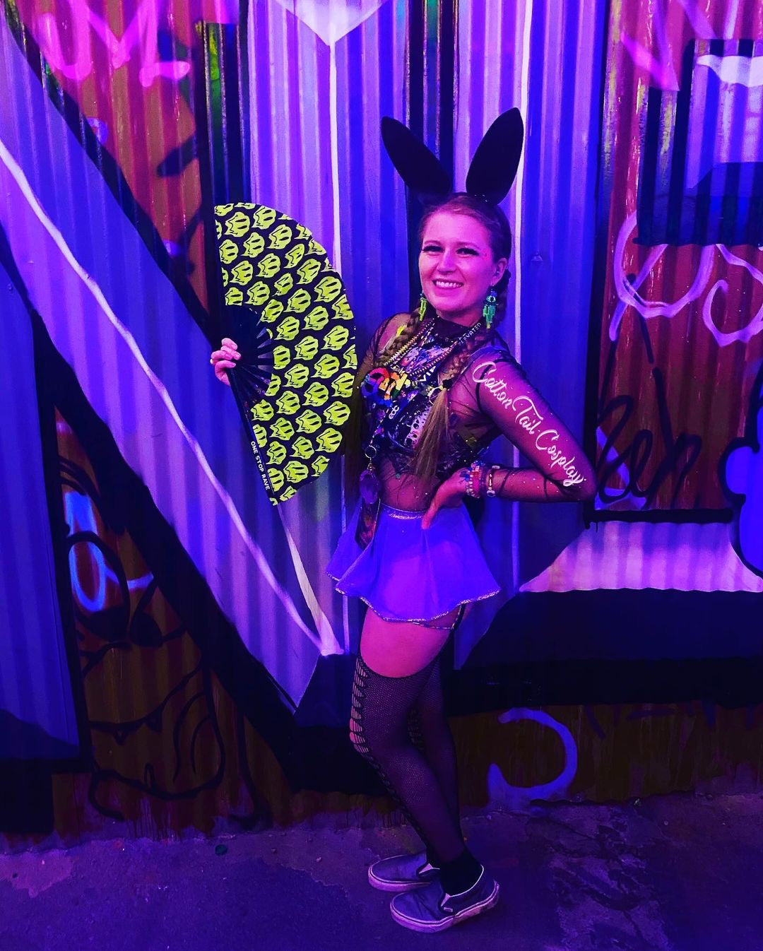 Stay Trippy hand fan held at festival by woman in bunny ears rave outfit.