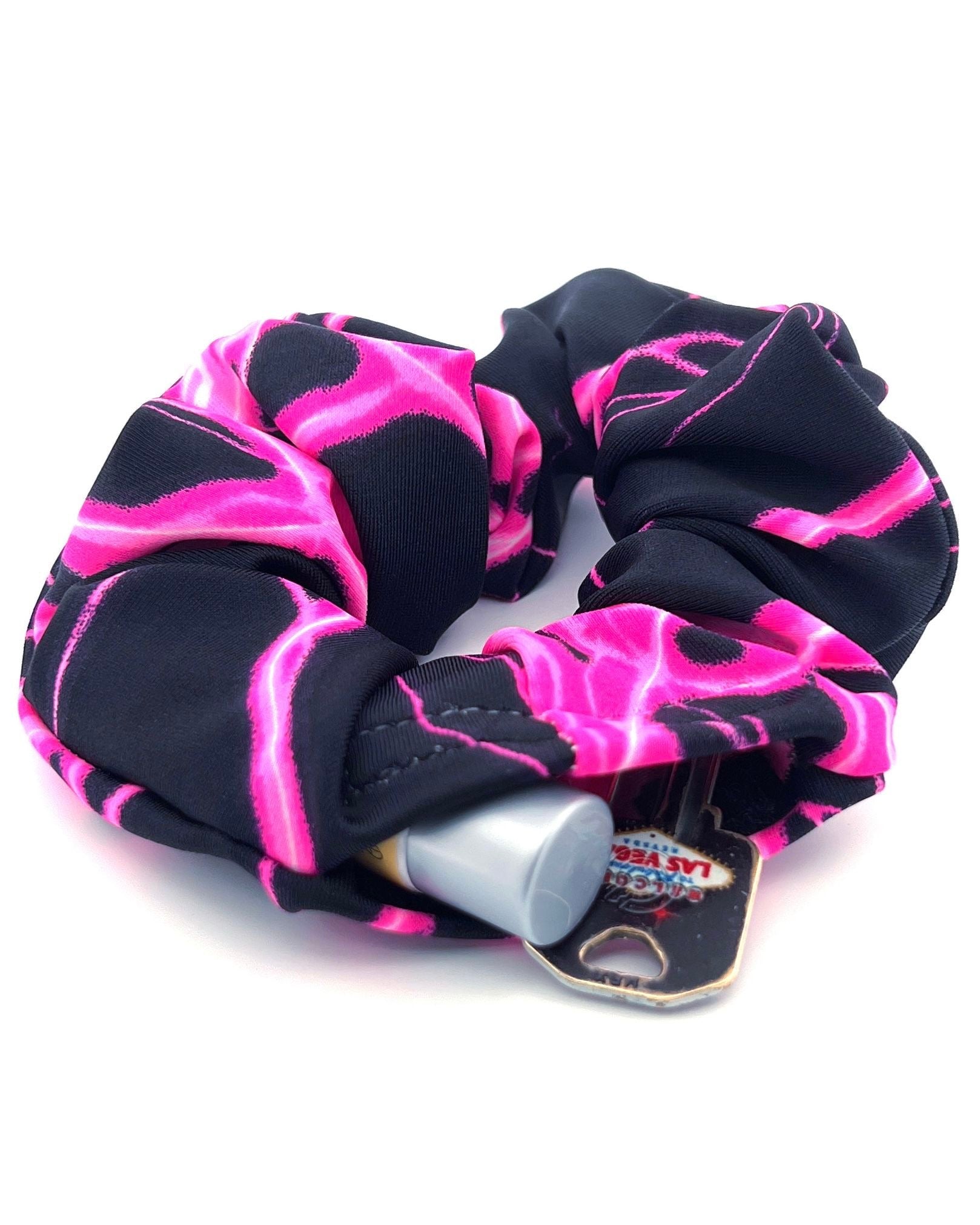 Pink Surge Stashie scrunchie hair tie with hidden Velcro® pocket opened on wrist with pink lighting bolts with a black background four way stretch polyester fabric.